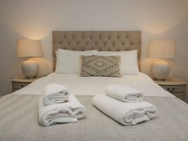 Una cama bien hecha con un cabecero capitonado, dos lámparas de noche y un cojín decorativo estampado.