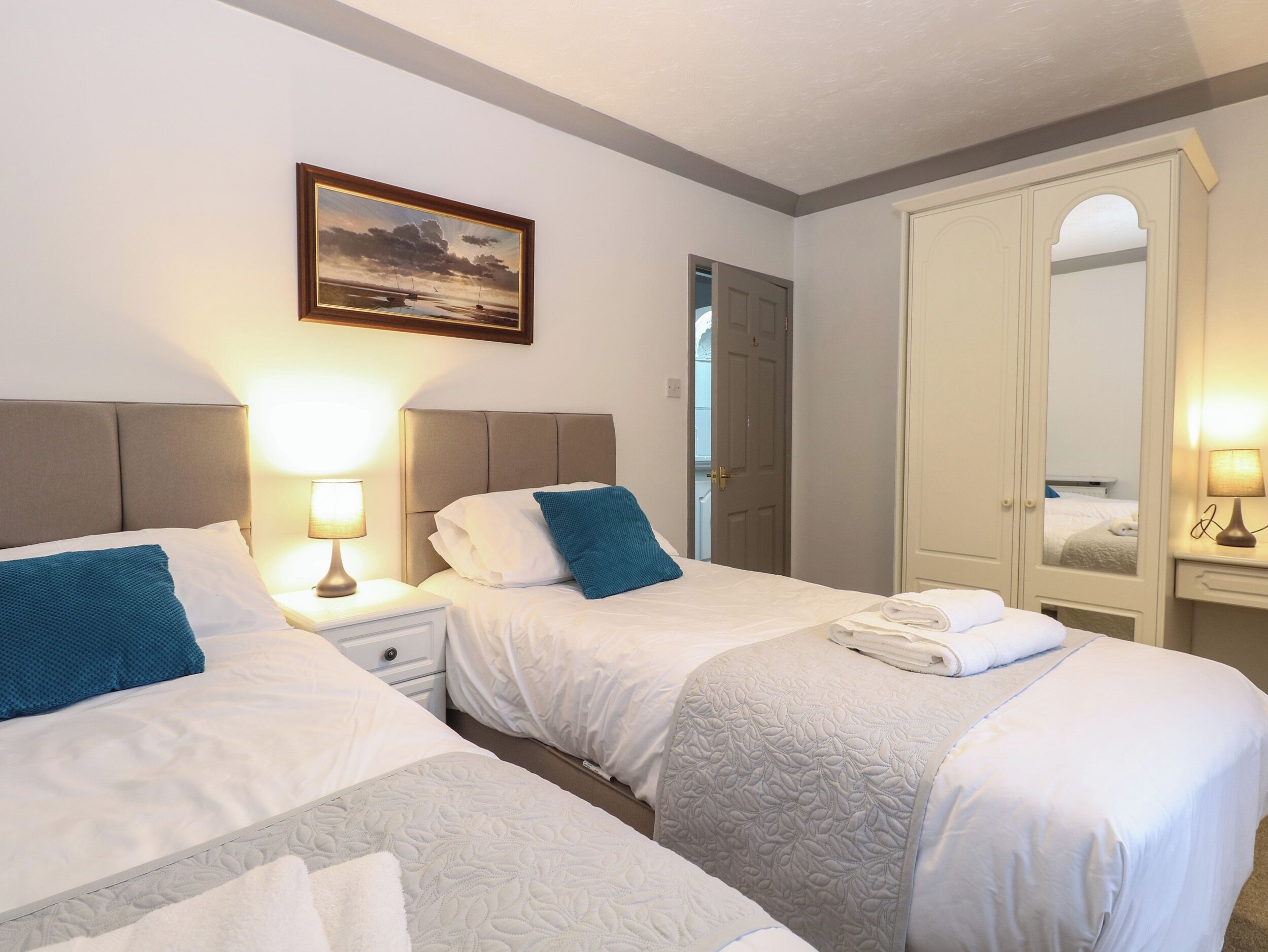 A hotel room with two beds, a painting on the wall, a wardrobe, and a mirror.