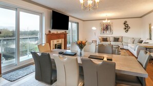 A modern living room with a dining area, large windows, a fireplace, and a chandelier. - White Gables (Norwich)