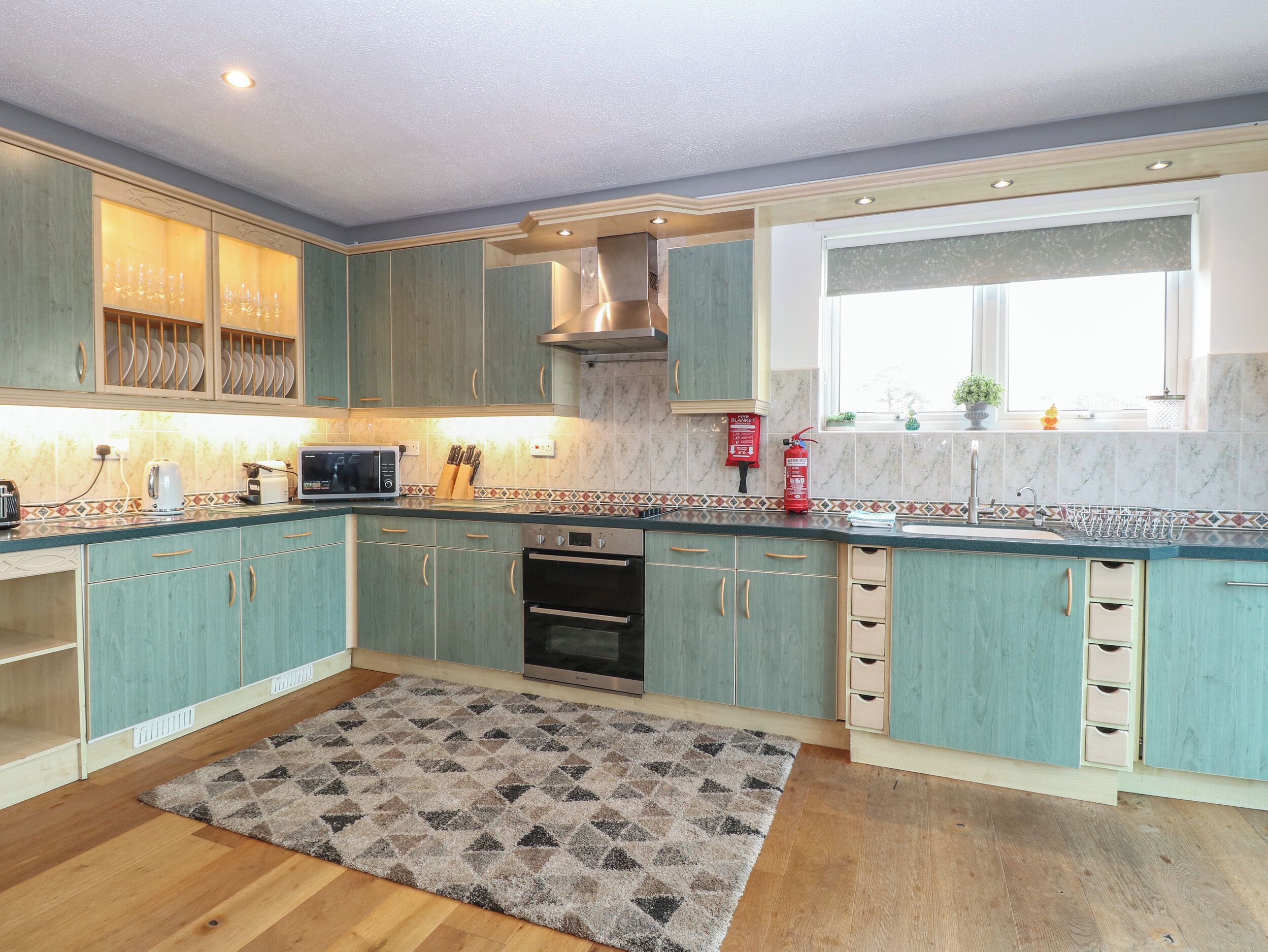 A modern kitchen with teal cabinets, a microwave, oven, and a window with a view.