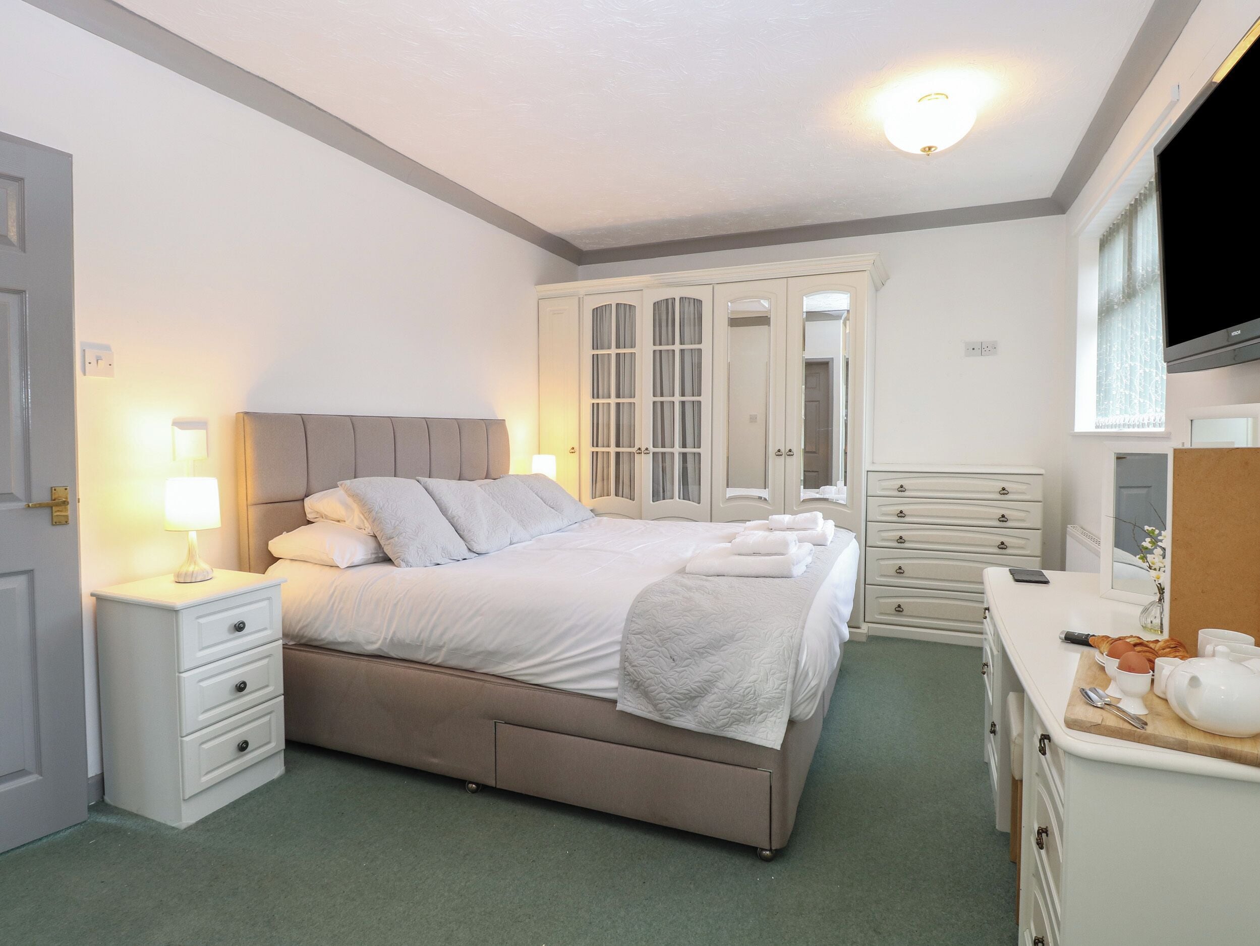 Een netjes ingerichte slaapkamer met een bed, nachtkastjes, een dressoir en een spiegel.