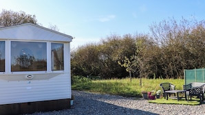 A mobile home with a large window, a gravel driveway, and outdoor seating.