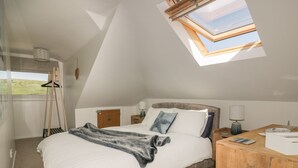 A bedroom with a skylight, a bed with a blanket, a wooden nightstand, and a hanging light fixture. - Atlantic View (Newquay)