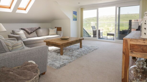 A spacious living room with a sofa, a coffee table, and a view of a balcony with outdoor seating. - Atlantic View (Newquay)