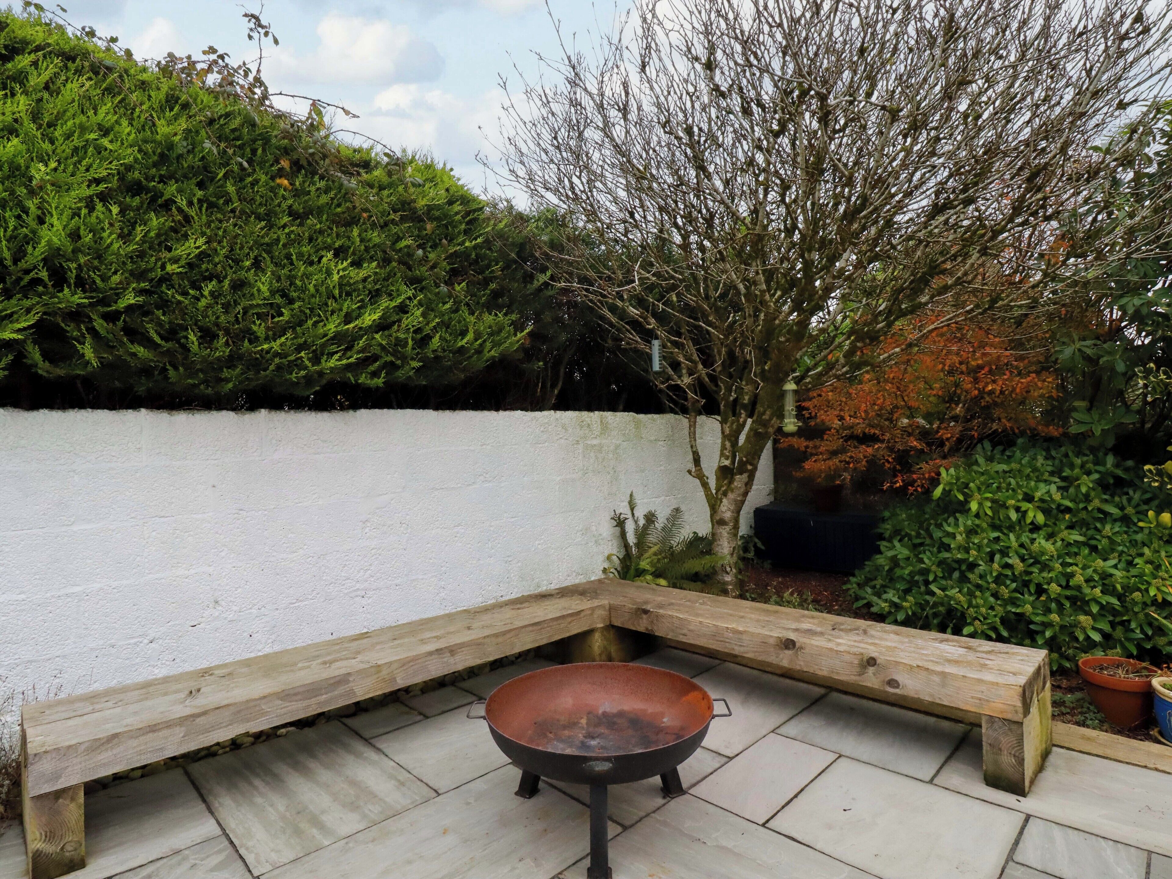 A corner with a metal fire pan, a wooden bench, and a white wall.