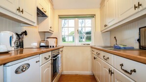 A kitchen with white cabinets, wooden countertops, a window, and a view of the outdoors. - The Coach House (Camelford)