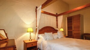 A bedroom with a four-poster bed, two bedside tables with lamps, a wooden wardrobe, and a chair. - The Coach House (Camelford)