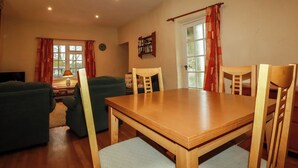 A dining area with a wooden table and chairs, a sofa, and a bookshelf. - The Coach House (Camelford)