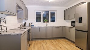A modern kitchen with grey cabinets, a stainless steel refrigerator, a microwave, and a window with a view of the outside. - 8 Sea Way (Bognor Regis)