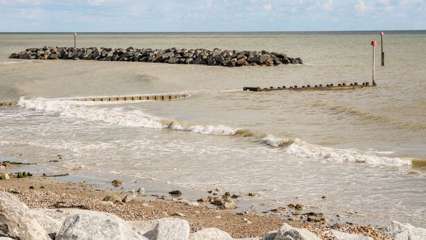 A rocky shoreline with waves crashing onto the beach, a breakwater, and a distant view of the sea. - 8 Sea Way (Bognor Regis)