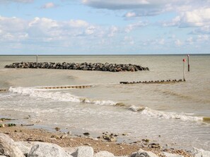 A rocky shoreline with waves crashing onto the beach, a breakwater, and a distant view of the sea. - 8 Sea Way (Bognor Regis)