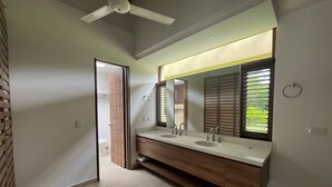 Ein modernes Badezimmer mit einem großen Spiegel, zwei Waschbecken, einem Holz-Waschtisch und einem Deckenventilator.