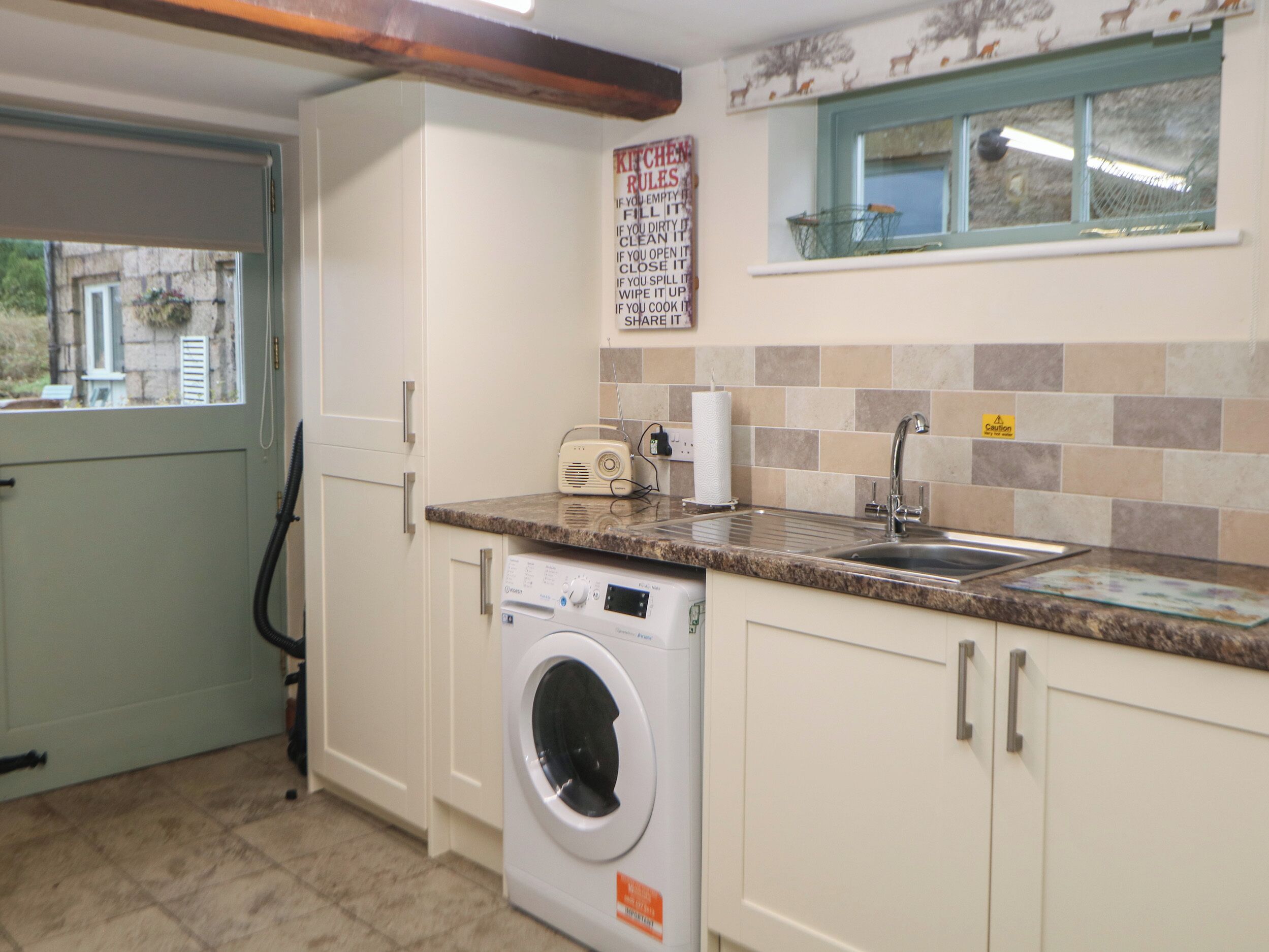 A compact kitchen with a washing machine, a sink, and a window with a view of the outside.
