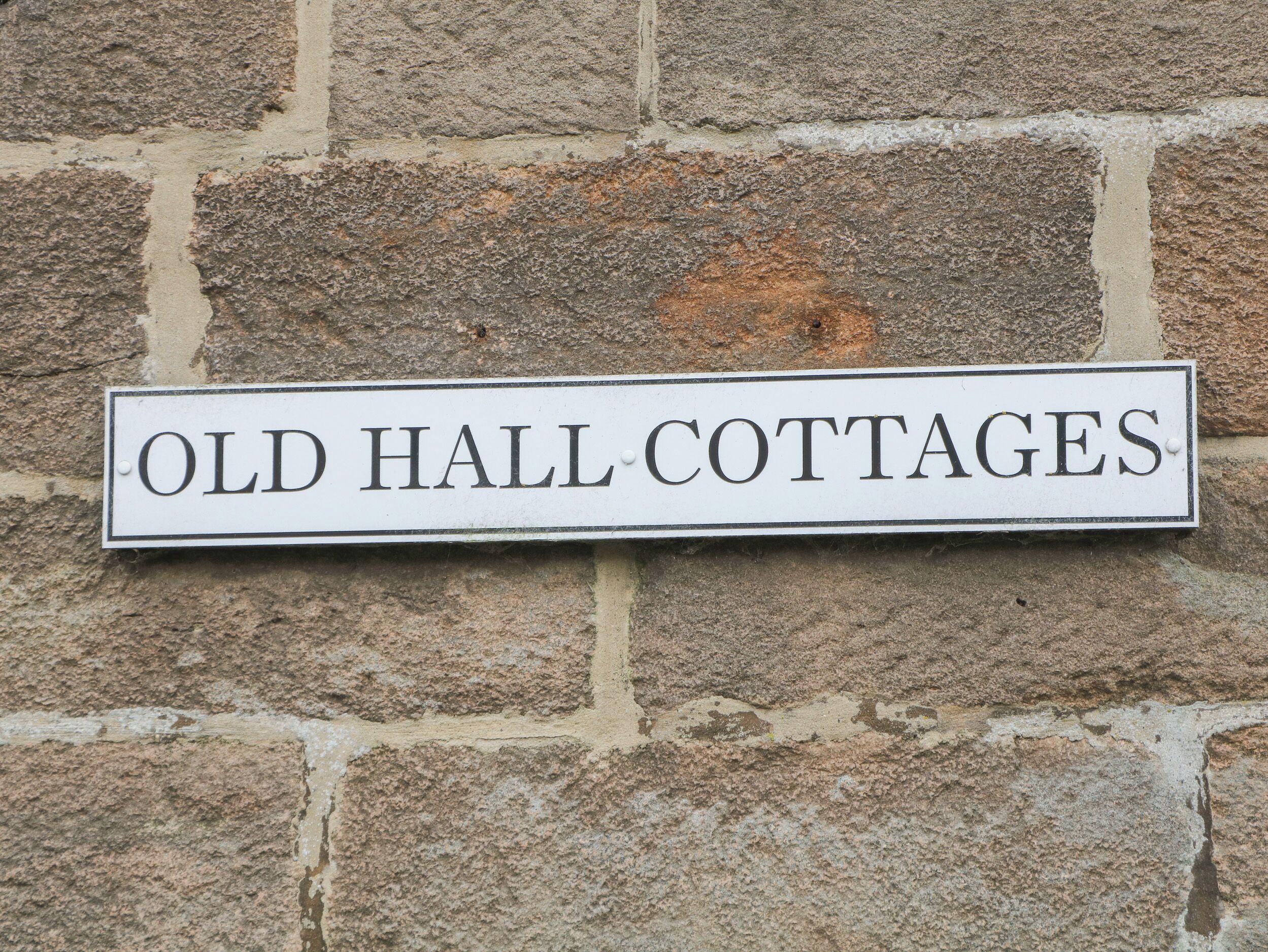 A sign reading "Old Hall Cottages" mounted on a stone wall.