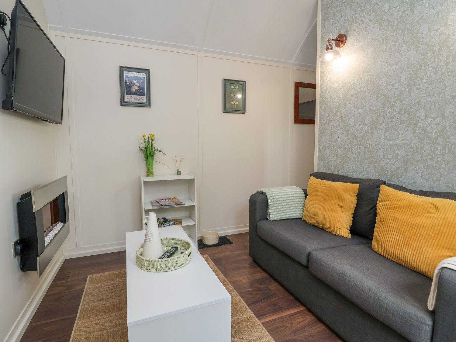 A modern living room with a grey sofa, white coffee table, and a flat-screen TV mounted on the wall.