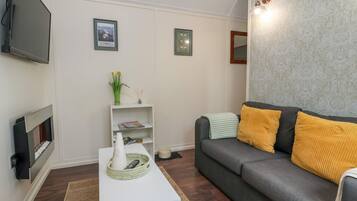 A modern living room with a grey sofa, white coffee table, and a flat-screen TV mounted on the wall.