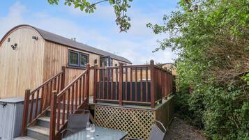 A wooden building with a deck, outdoor seating, and a staircase leading to the entrance.