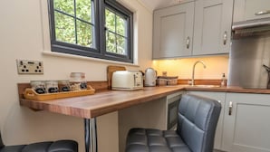 Une cuisine avec un plan de travail en bois, deux tabourets de bar en cuir noir, un réfrigérateur en acier inoxydable et une fenêtre donnant sur un espace verdoyant.