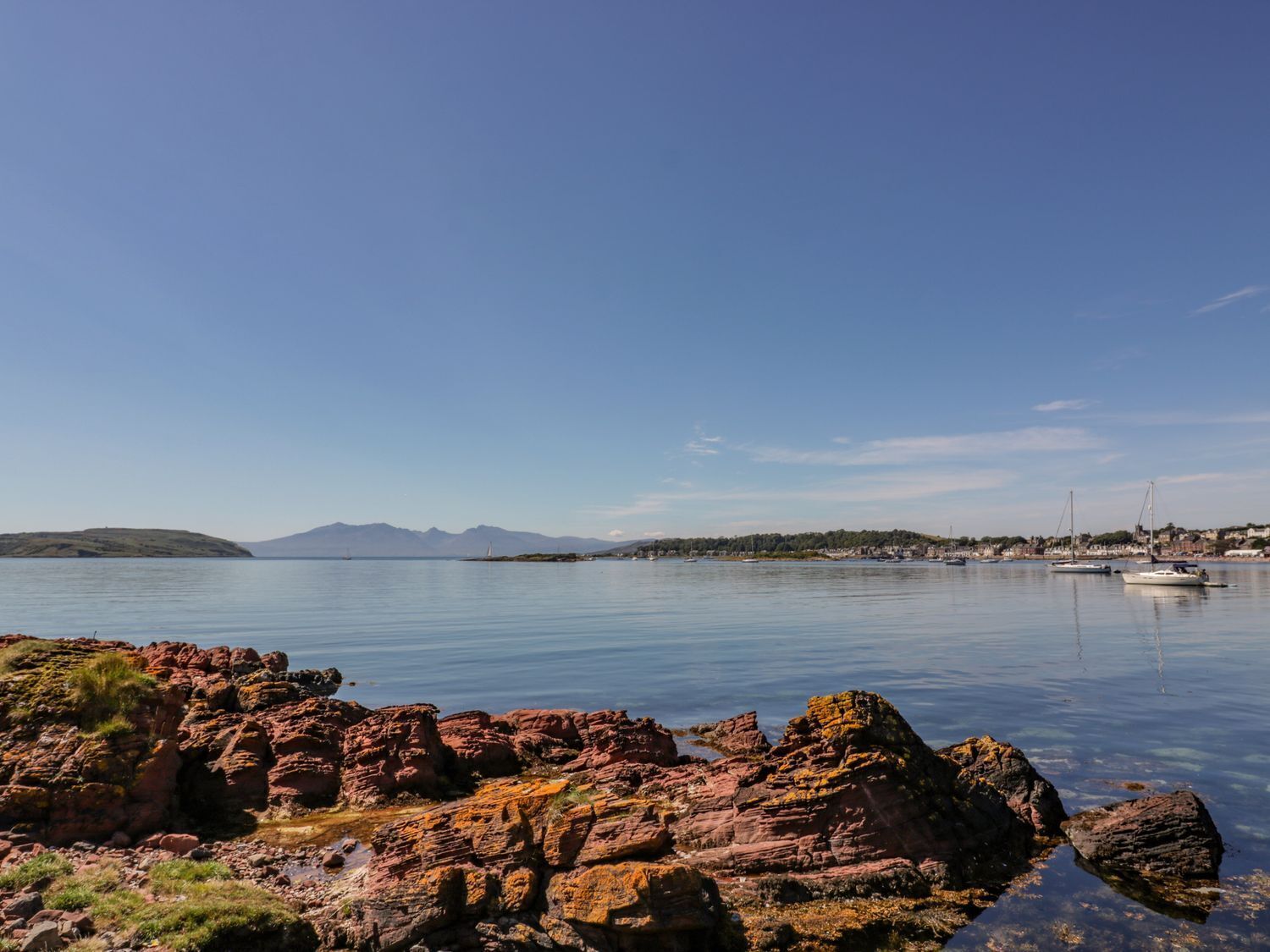 A coastal scene with rocky outcrops, calm water, and distant mountains.