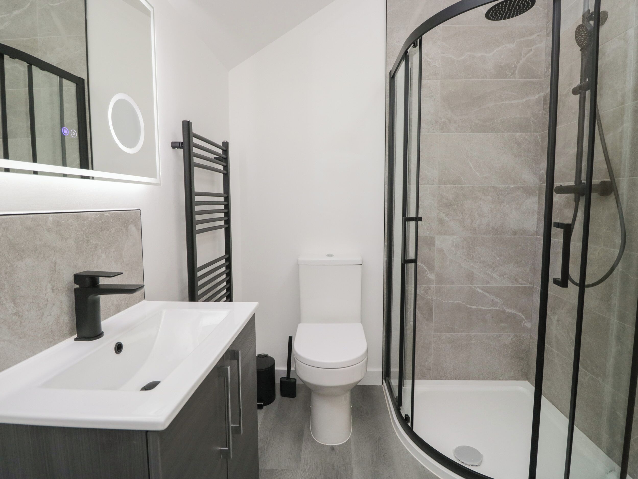 A modern bathroom with a white sink, toilet, and glass-enclosed shower.