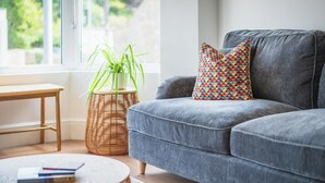 A modern living room with a grey sofa, a wicker side table, a round coffee table, and a potted plant. - Hoheck (Pwllheli)