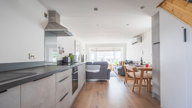 A modern kitchen with a central island, wooden flooring, and a dining area with a table and chairs. - Hoheck (Pwllheli)