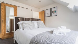 A modern bedroom with a large bed, a wooden wardrobe, a mirror, and framed artwork on the wall. - Hoheck (Pwllheli)