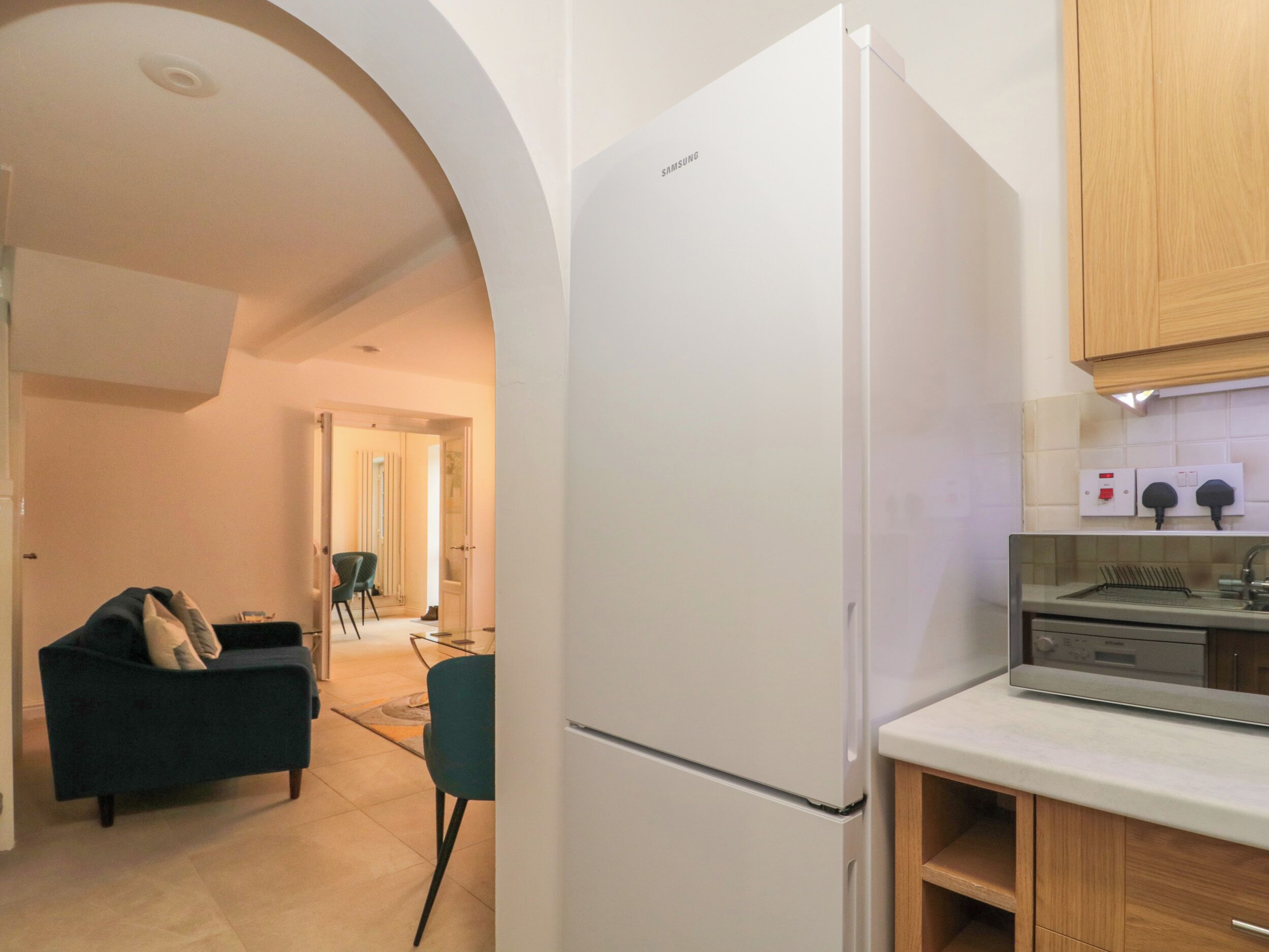 A modern kitchen with a white refrigerator, wooden cabinets, and a dining area with a dark sofa and chairs.