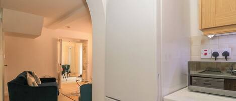 A modern kitchen with a white refrigerator, wooden cabinets, and a dining area with a dark sofa and chairs.