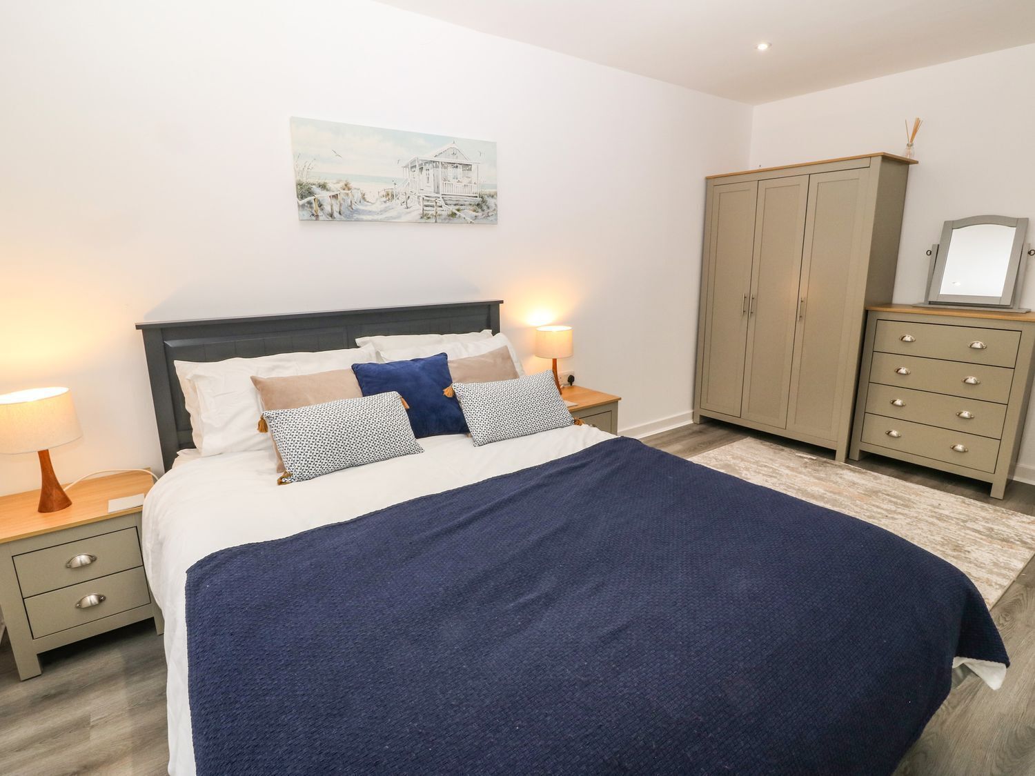 A neatly arranged bedroom with a bed, bedside tables, a dresser, and a painting on the wall.