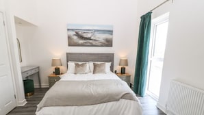 Une chambre à coucher avec un lit, deux tables de chevet, une lampe, un tableau et une fenêtre avec des rideaux.