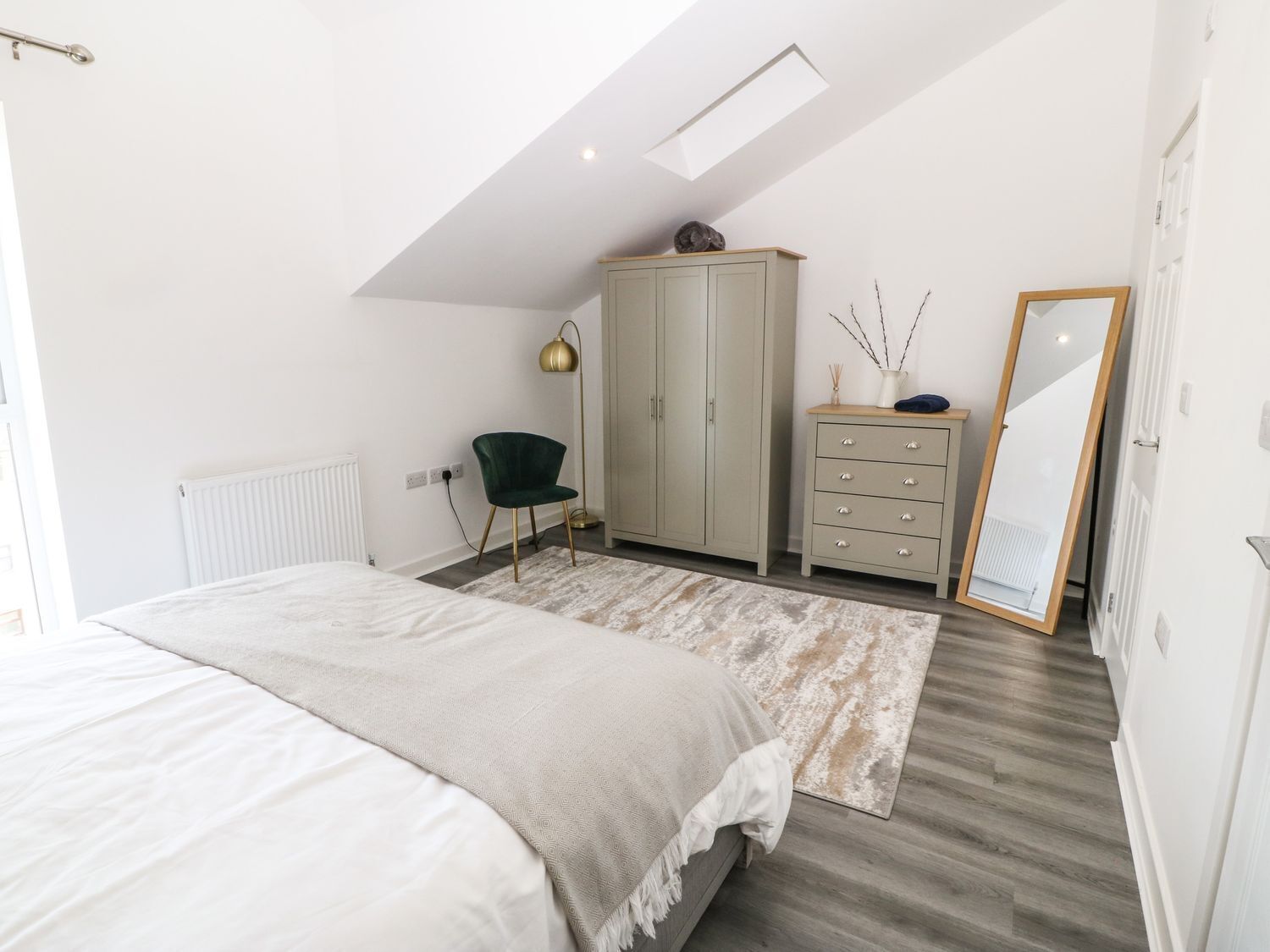 A bedroom with a bed, a dresser, a chair, a floor lamp, and a mirror.
