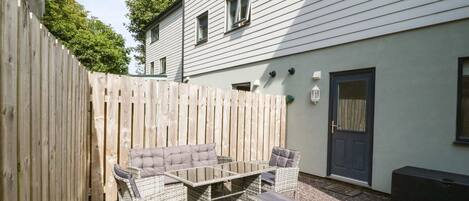 Une terrasse avec des meubles en osier, une table et des chaises.