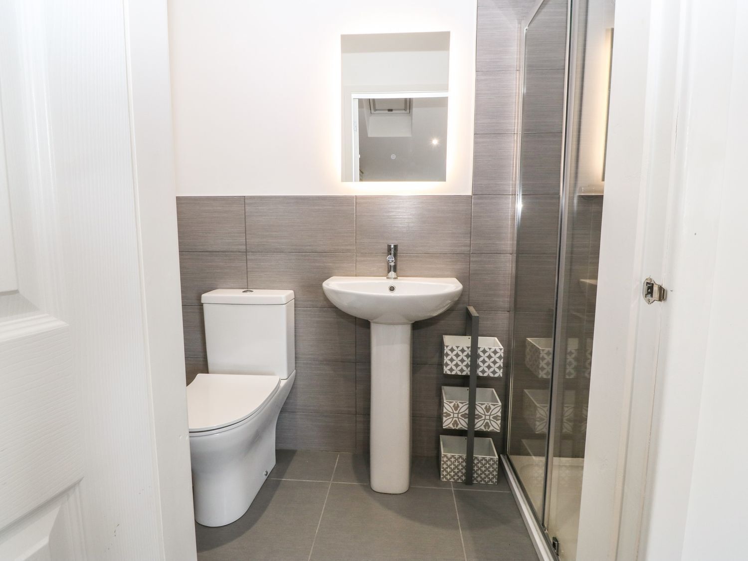 A compact bathroom with a toilet, pedestal sink, and a glass shower enclosure.