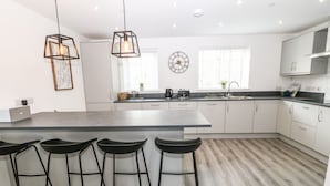 Une cuisine moderne dotée d’un îlot central, de tabourets de bar, de luminaires suspendus et d’une horloge au mur.