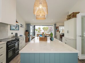 A modern kitchen with a central island, black appliances, and a wicker pendant light. - Chapel House (Rhosneigr)