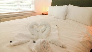 Ein ordentlich gemachtes Bett mit weißen Leinen und zwei Handtüchern, die zu einem Herzen arrangiert sind.