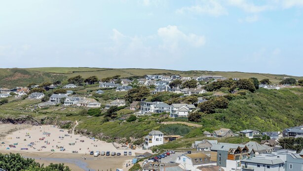 Un quartier résidentiel situé sur la côte, avec des maisons construites sur une colline, une plage de sable et des voitures garées.