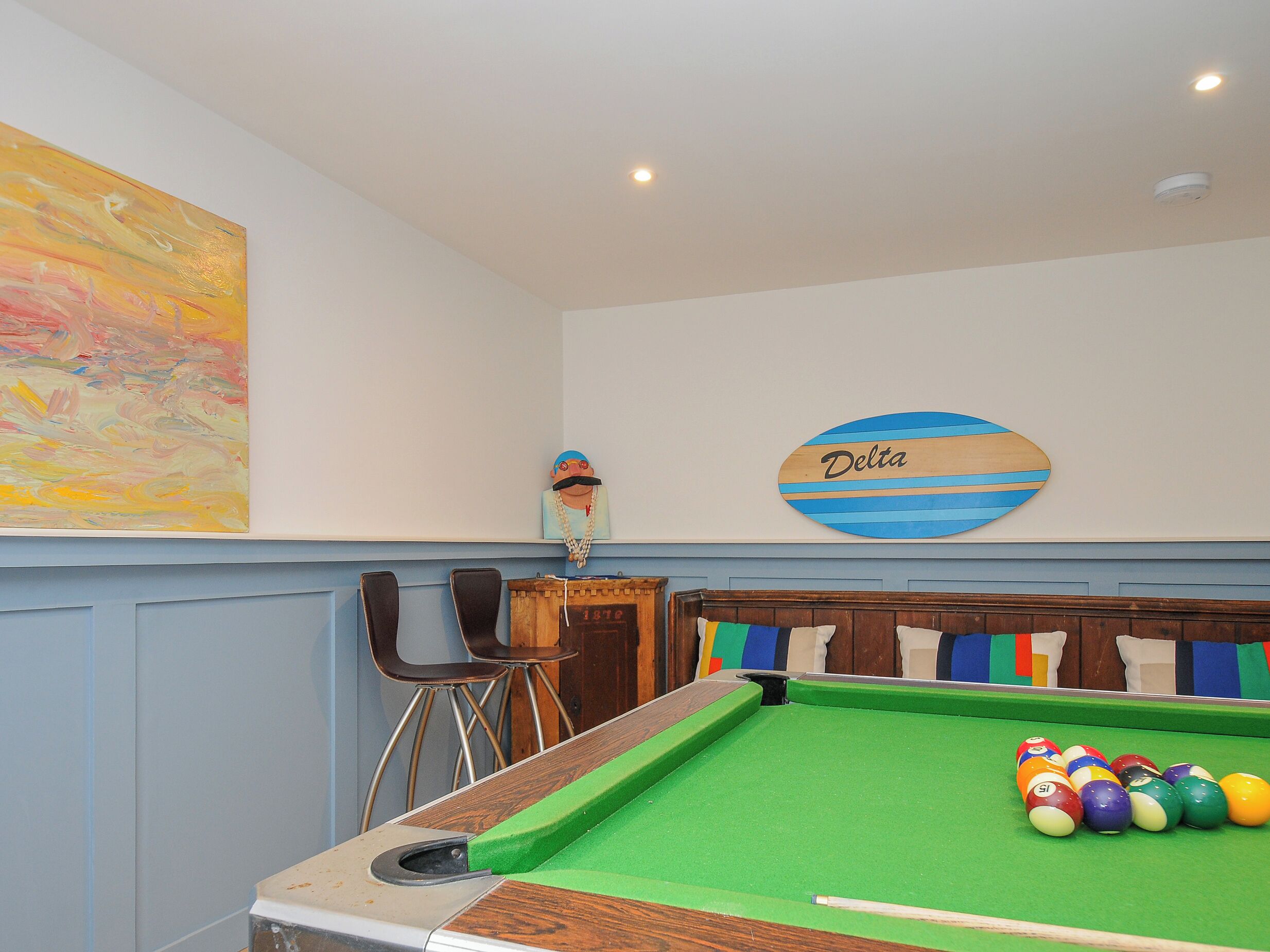 A pool table with colorful balls, a wooden sign with "Delta" on it, and a colorful abstract painting on the wall.