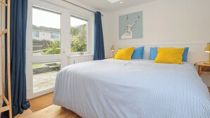 Une chambre avec un grand lit, une lucarne, une vue sur le jardin et un tableau au mur.