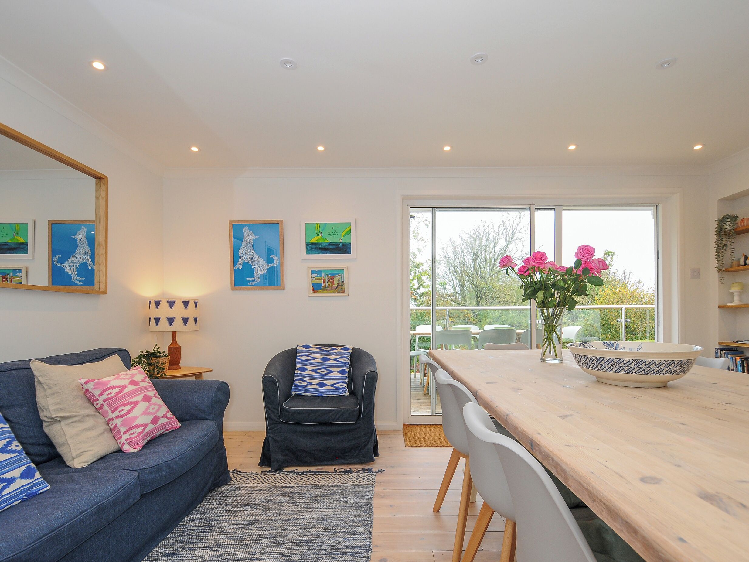 A modern living room with a sofa, armchair, dining table, and artwork on the walls.