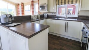 Eine kompakte Küche mit Mikrowelle, Toaster und Kaffeemaschine auf der Arbeitsfläche, weißen Schränken und einem Fenster mit Vorhängen.