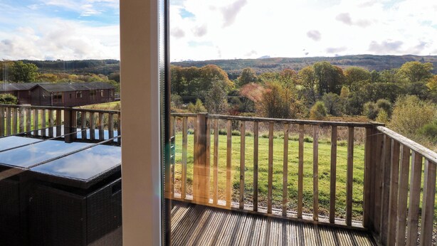 Ein Balkon mit Blick auf eine Wiese und Bäume, eine Holzterrasse und ein Gebäude im Hintergrund.