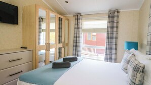 Ein Schlafzimmer mit Bett, Schminktisch, Fernseher und einem Fenster mit Vorhängen.