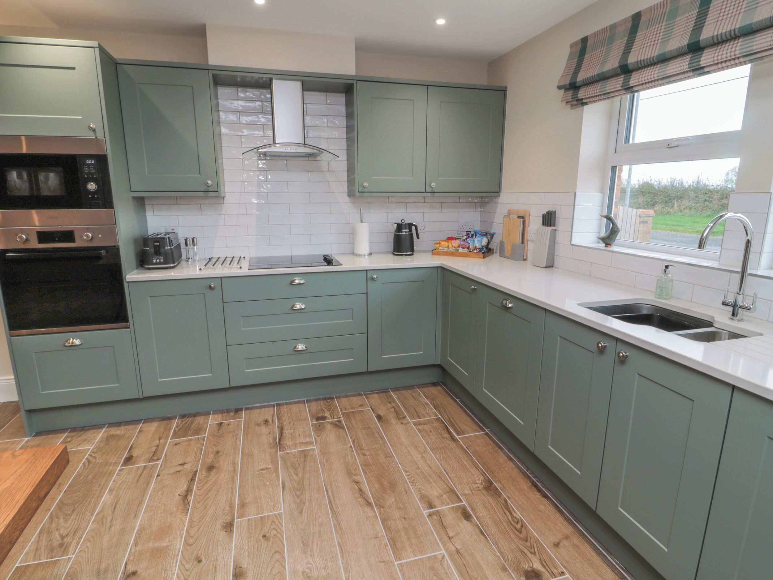 Une cuisine moderne avec des meubles de couleur vert clair, un four en acier inoxydable et un plancher en bois.