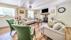 A living room with a sofa, armchairs, a fireplace, and a television. - Bodior Garden Cottage (Holyhead)