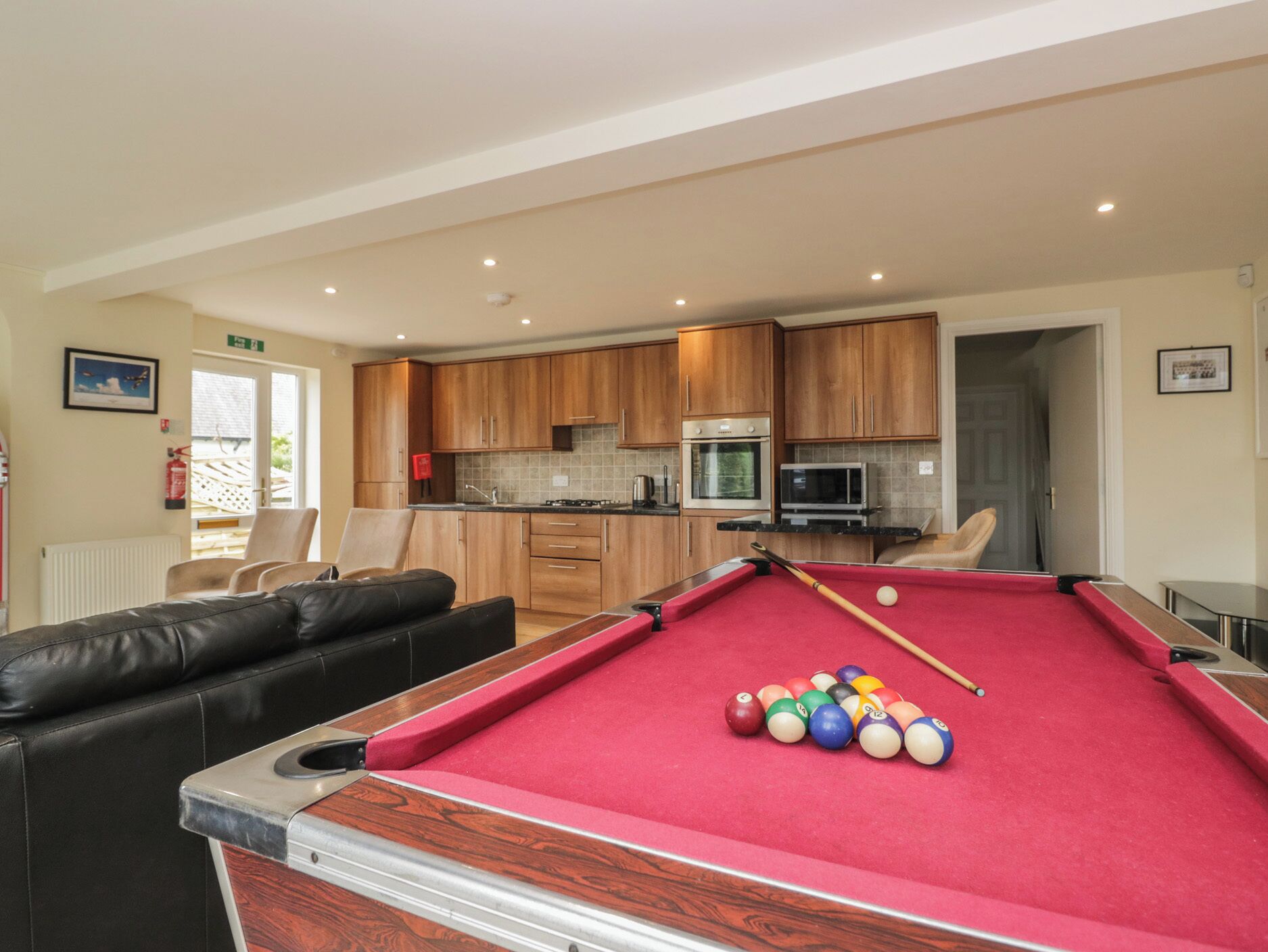 A pool table with balls, a sofa, and a kitchen area with wooden cabinets.