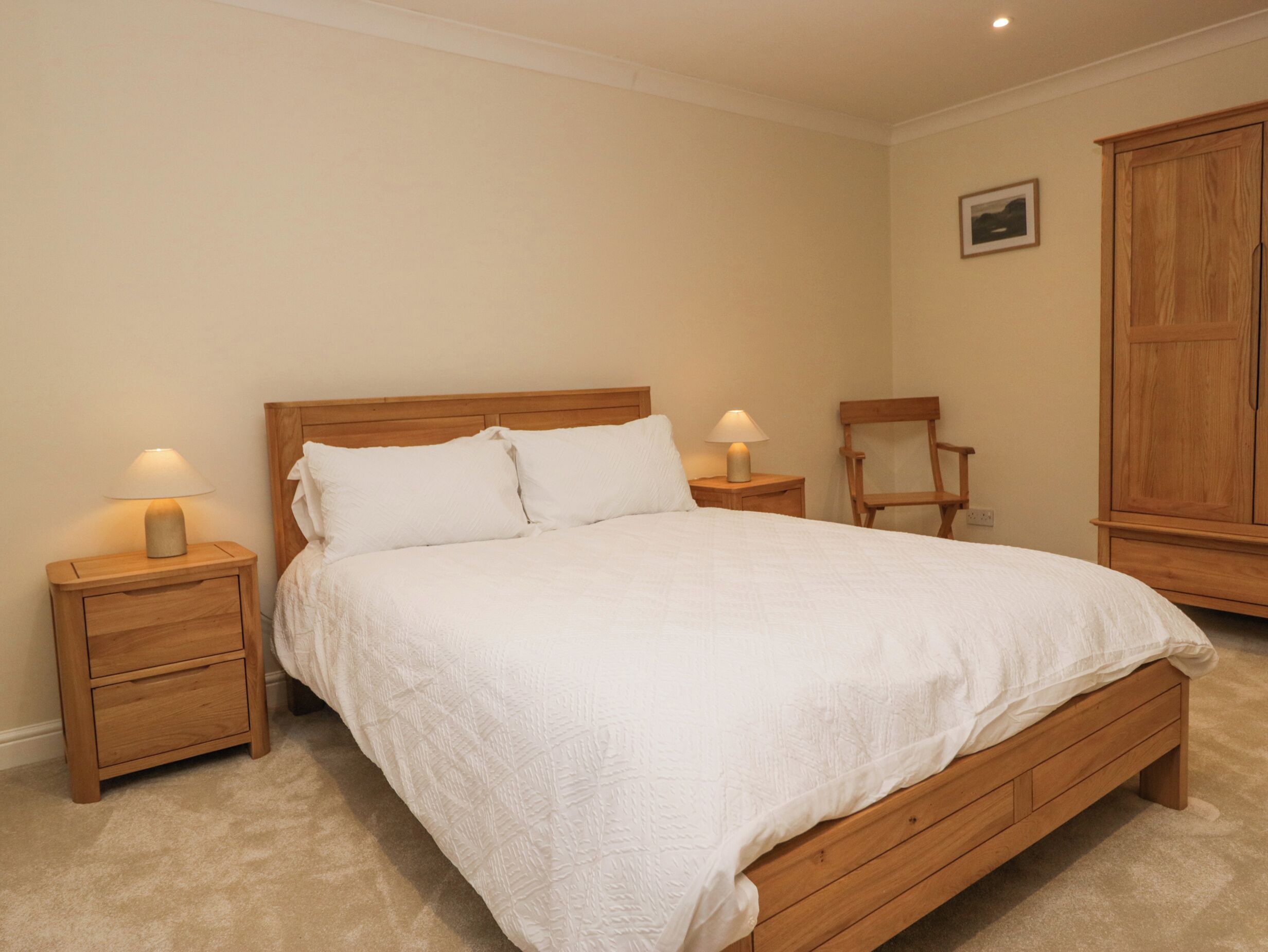 A bedroom with a wooden bed, two bedside tables with lamps, a wooden chair, and a wardrobe.