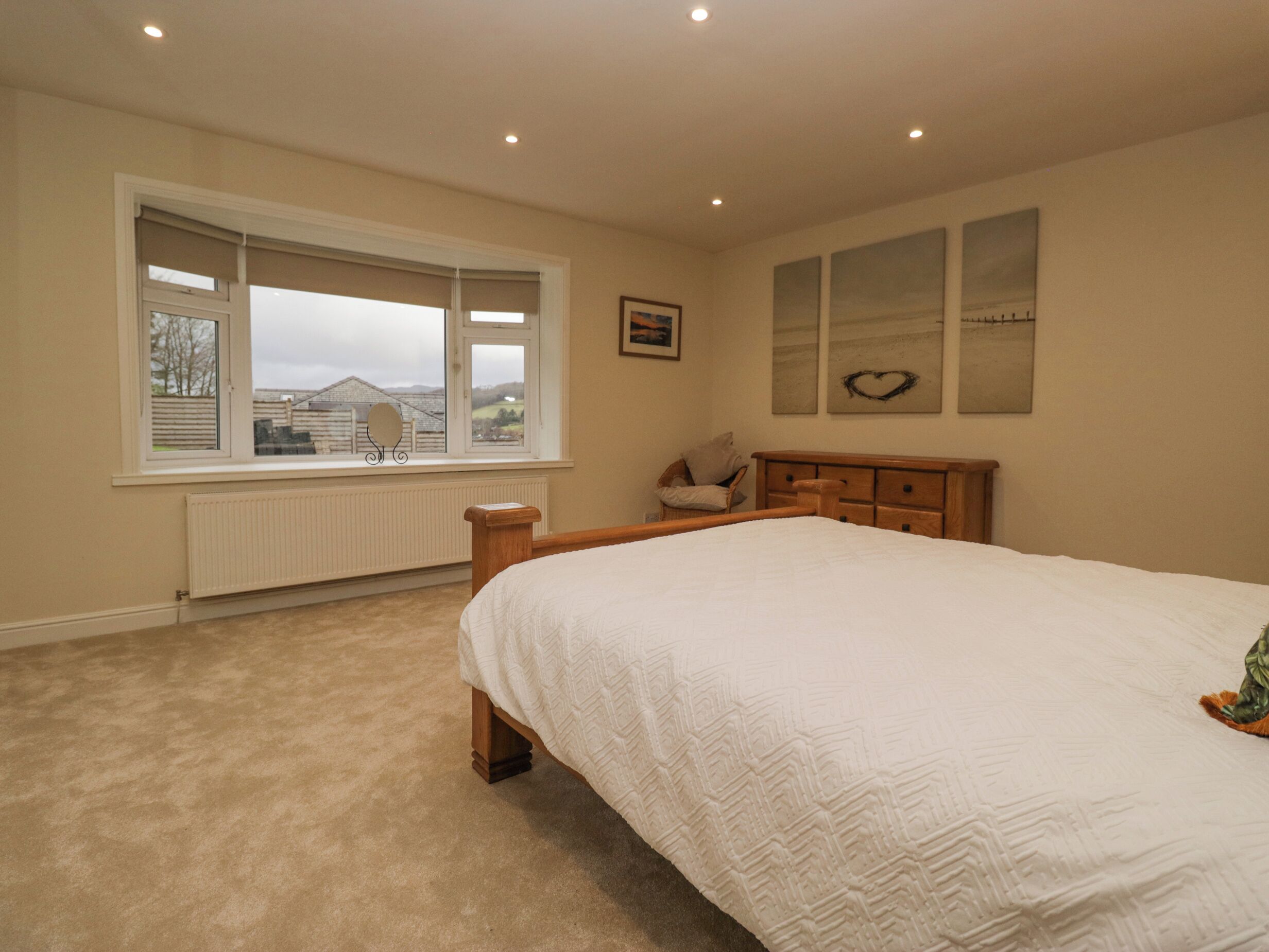 A bedroom with a large bed, a window with a view, a radiator, and a wooden dresser.