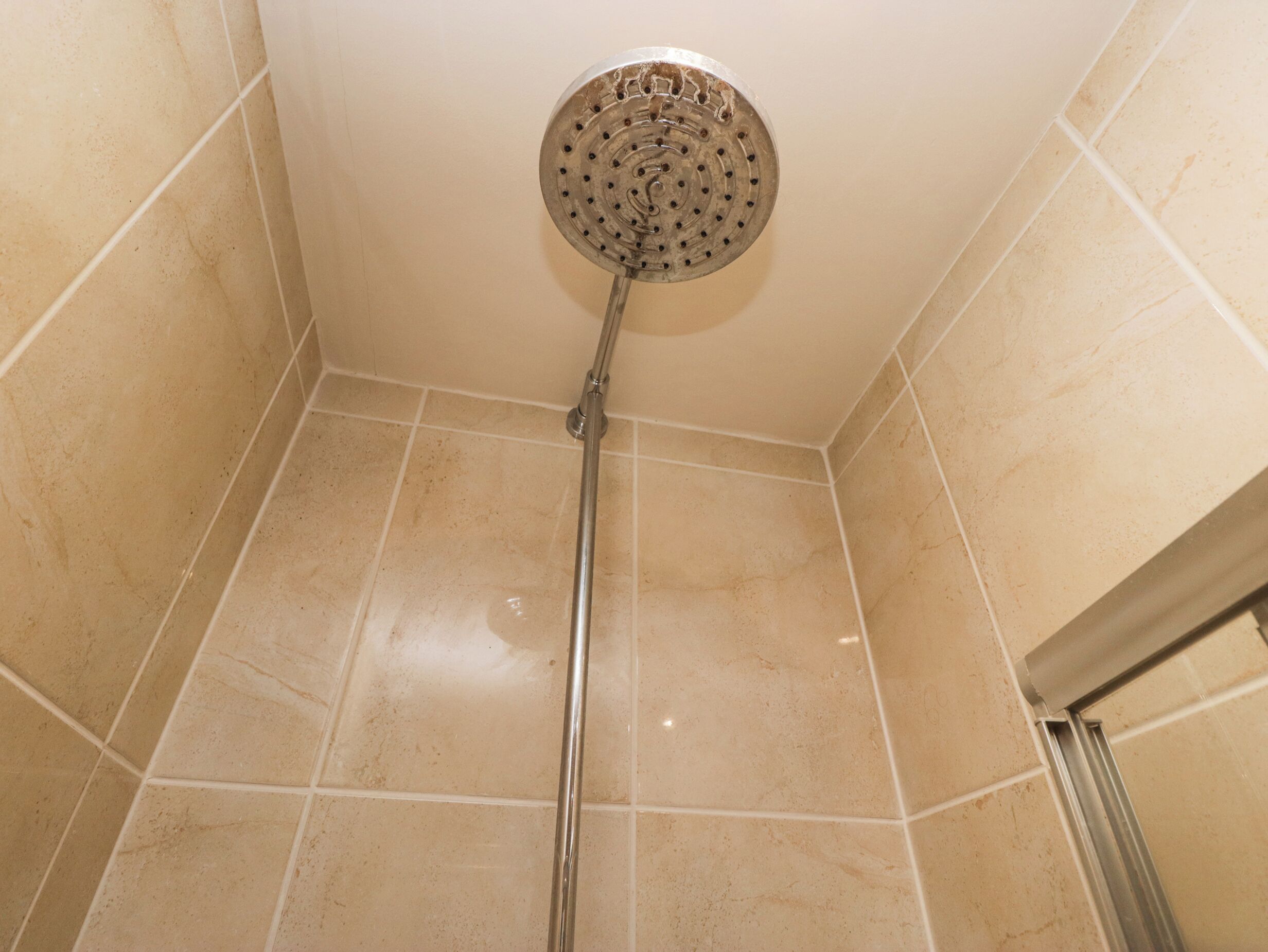Une douche avec un pommeau de douche amovible dans une salle de bain carrelée.